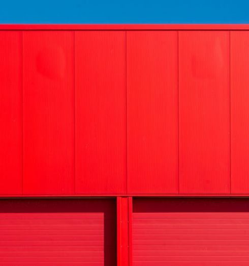 Outdoor Storage - Bright red garage doors of an industrial building against a clear blue sky, showcasing minimalism.