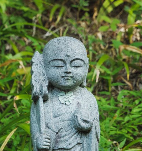 Rock Garden - A small stone statue stands peacefully surrounded by green foliage, symbolizing tranquility in nature.