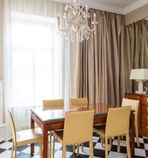 Art Deco Furniture - Dining table with chairs placed near window covered with curtains in kitchen with classic chandelier in apartment