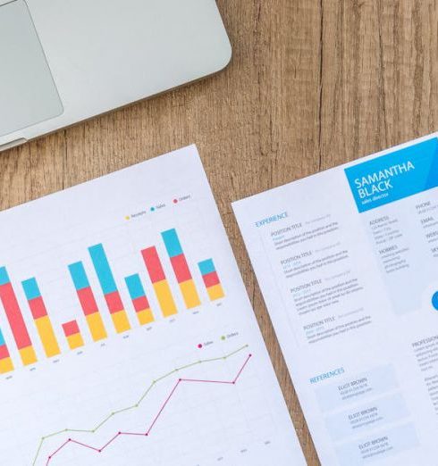 Business Plan - Top view of a laptop, charts, and resume on a wooden desk, showcasing business analysis and job application.