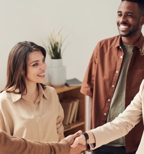 Business - Four colleagues smiling and shaking hands in a bright office setting.