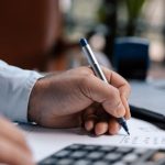 Financial Management - A person calculating finances with a calculator and pen on a desk indoors.