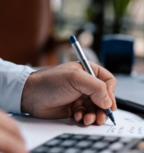 Financial Management - A person calculating finances with a calculator and pen on a desk indoors.