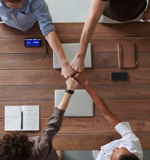 Business Model - A diverse group of professionals engaging in a teamwork celebration with a fist bump over a wooden table indoors.