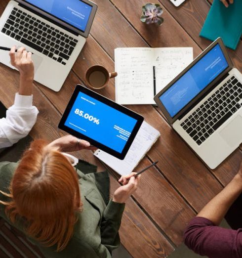 Employees - Diverse team discussing business strategies with laptops and tablets at a wooden table.