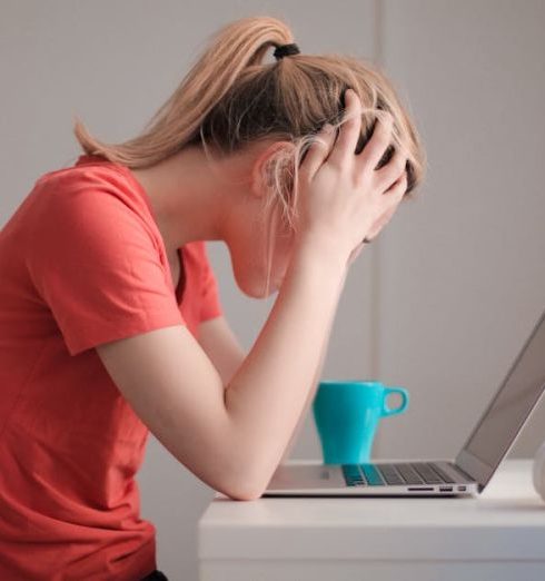 Stress - Young woman feeling stressed while studying at home with a laptop and coffee cup.