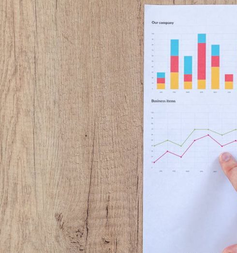 Metrics - Hand analyzing business graphs on a wooden desk, focusing on data results and growth analysis.