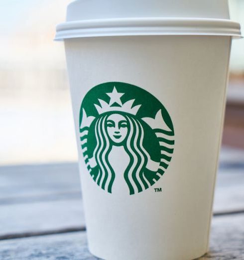 Branding - A disposable coffee cup with a lid outdoors on a wooden table, featuring a popular global logo.