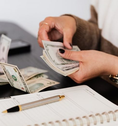 Budgeting - Close-up of person counting cash with notepad on desk, indicating financial tasks.