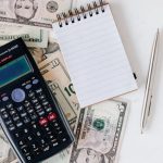 Budget - Flat lay of US dollar bills with calculator and notebook for budgeting.