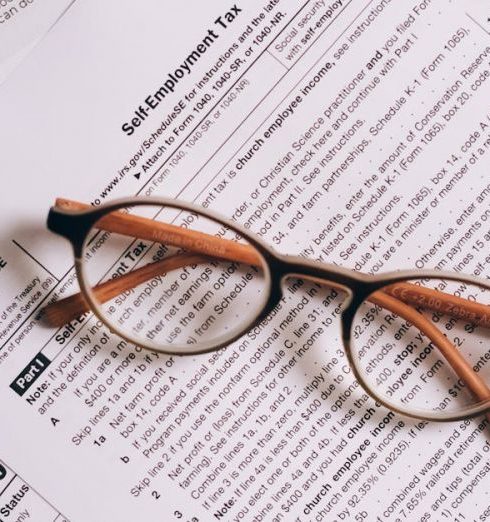 Accounting Software - Overhead view of tax documents and eyeglasses on a laptop keyboard, ideal for finance or accounting themes.