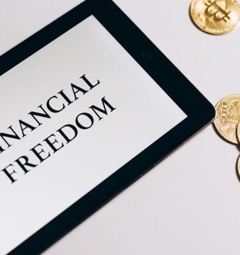 Financial Goals - Tablet showing 'Financial Freedom' with gold bitcoins nearby, symbolizing cryptocurrency investment.