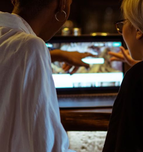 Break-Even Point - Two women browsing a laptop together at a cozy café bar, seen from behind in a relaxed atmosphere.