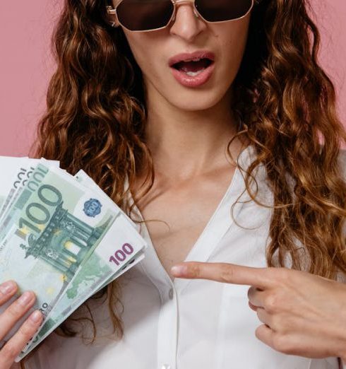 Cash Flow Statements - Young woman in sunglasses holding euro banknotes and pointing, pink background