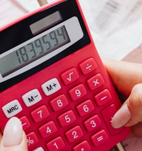 Costs - A person calculating finances on a red calculator surrounded by documents.