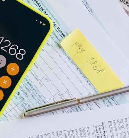 Financial Statements - Tax documents and currency with a smartphone calculator on a pink background.