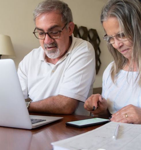 Retirement Plan - Senior couple working together on documents with laptop and phone at home.