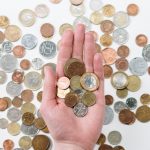 Overhead Costs - An open hand holds various coins on a white surface, symbolizing finance and currency exchange.