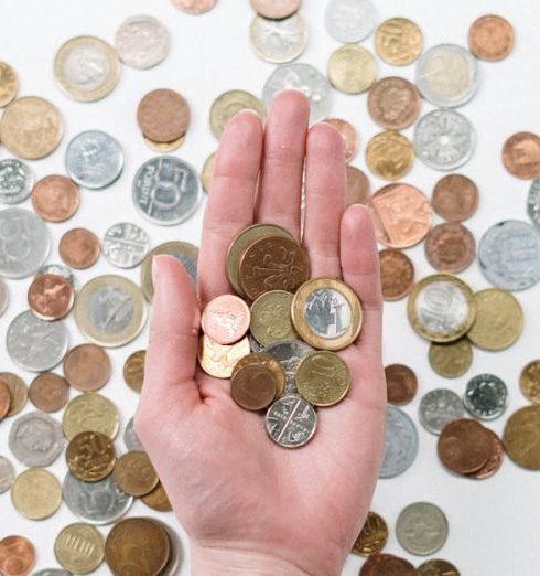 Overhead Costs - An open hand holds various coins on a white surface, symbolizing finance and currency exchange.