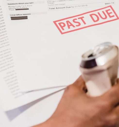 Bad Debt - Man holding bills labeled 'Past Due' and a drink can, lying on a sofa.