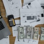 Gross Revenue - Overhead view of financial documents, cash, and technology on a wooden desk.