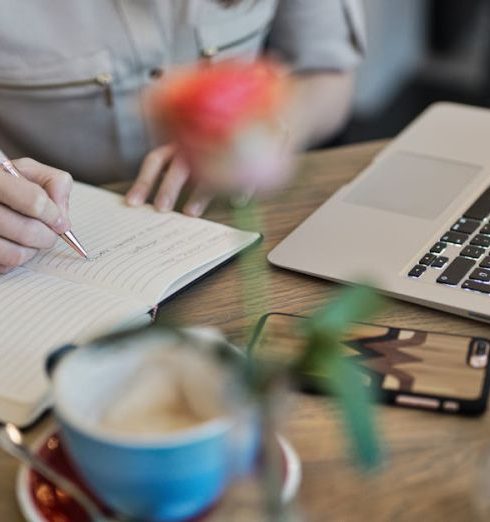 Content Marketing - Woman writing in a notebook with a laptop and coffee cup on a desk. Ideal for workspace inspiration.