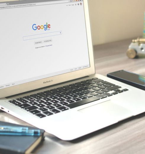 SEO - A neat workspace featuring a laptop displaying Google search, a smartphone, and a notebook on a wooden desk.