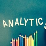 Email Marketing - Colored pencils and letters spelling 'ANALYTICS' on a textured background with a hand.