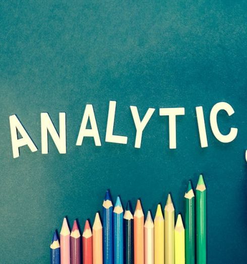 Email Marketing - Colored pencils and letters spelling 'ANALYTICS' on a textured background with a hand.