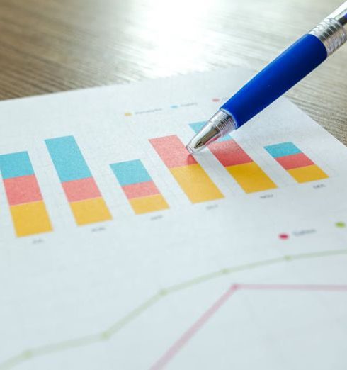 Marketing Metrics - Detailed close-up of a hand pointing at colorful charts with a blue pen on wooden surface.