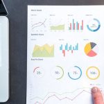 Data Analytics - Detailed charts and graphs on a document next to a laptop, representing data analysis.