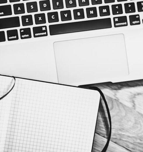 Landing Page - Black and white image of a workspace featuring a laptop, notebook, pen, and coffee cup.