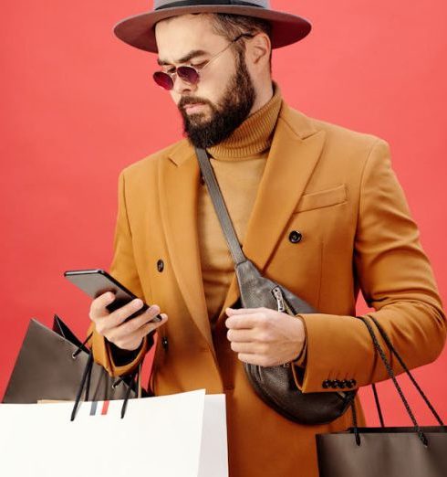 Loyalty Program - Fashionable man with shopping bags using smartphone. Stylish look with beard, hat, and sunglasses.