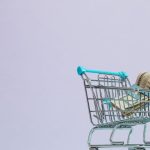 Marketing Budget - A close-up of a mini shopping cart with rolled cash on a pastel background. Ideal for finance and ecommerce themes.