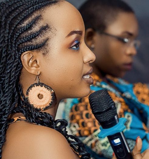 Communication Skills - Confident young woman speaks into a microphone at an indoor event, engaging with the audience.