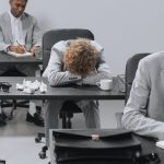 Team Meetings - Tired employees in a modern office setting showing signs of workplace exhaustion.