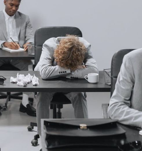 Team Meetings - Tired employees in a modern office setting showing signs of workplace exhaustion.