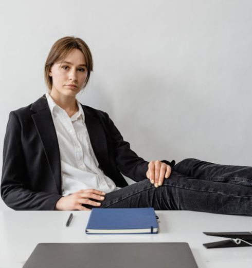 Leadership Style - Confident young woman in a business suit relaxing with feet on desk in modern office.