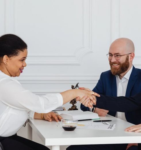 Delegation - Business meeting with diverse professionals in office attire shaking hands.