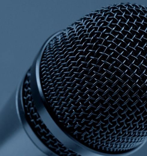 Public Speaking - A detailed close-up of a microphone with a blue monochrome background, highlighting its intricate mesh design.