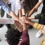 Team Building - A diverse group of professionals joins hands in a team-building exercise indoors.