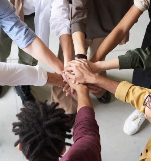 Team Building - A diverse group of professionals joins hands in a team-building exercise indoors.