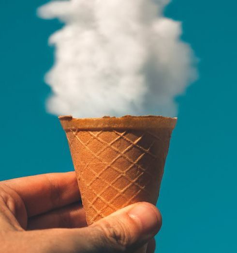 Creativity - Hand holding an ice cream cone with a cloud effect against a clear sky background.