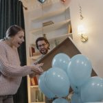 Expectations - Friends joyfully celebrate a gender reveal with blue balloons indoors.