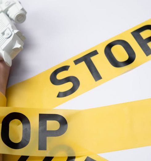 Conflict Prevention - A white toy gun held by a hand wrapped in yellow stop tape on a white background, conveying a message of caution.