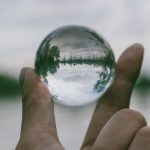 Transparency - A hand holding a transparent glass sphere outdoors, showcasing an inverted reflection of the landscape.