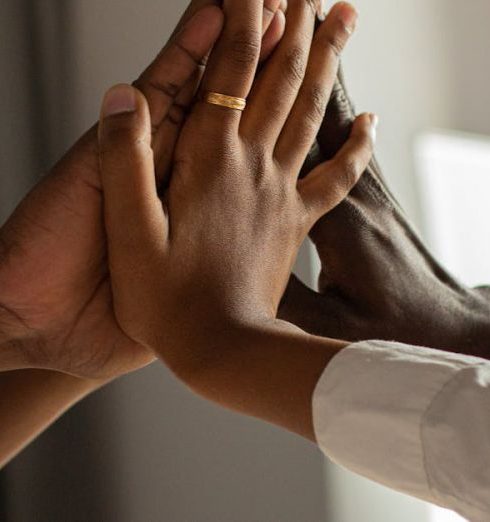 Initiative - Diverse hands meeting in a high five, symbolizing teamwork and unity in a modern office.