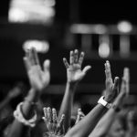 Praise - A group of people raising hands in a black and white concert setting, showing unity and celebration.