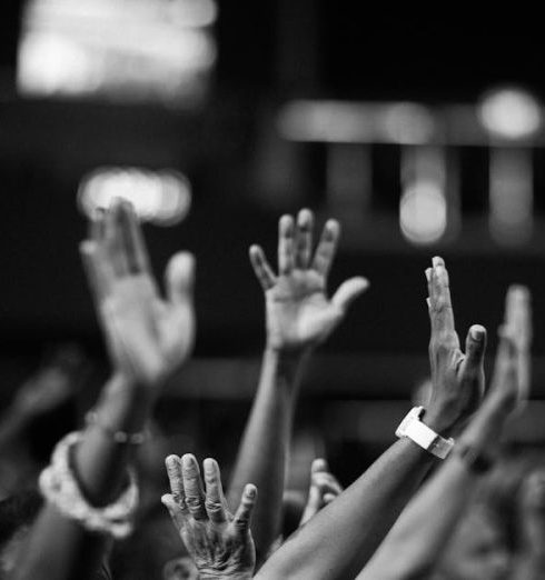 Praise - A group of people raising hands in a black and white concert setting, showing unity and celebration.