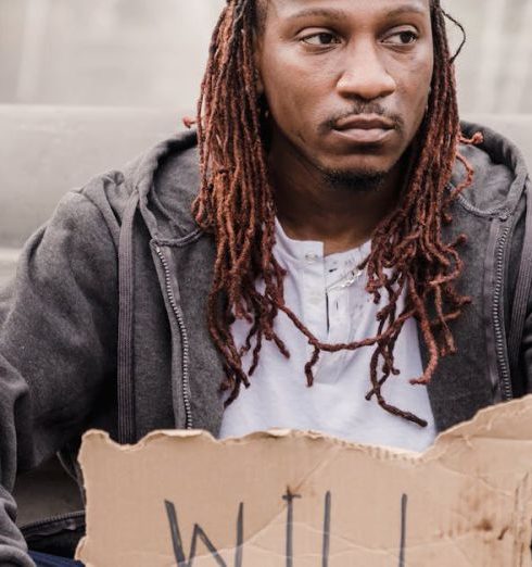 Difficult Times - A man sits outdoors holding a cardboard sign reading 'Will Work For Food', signifying homelessness and poverty.